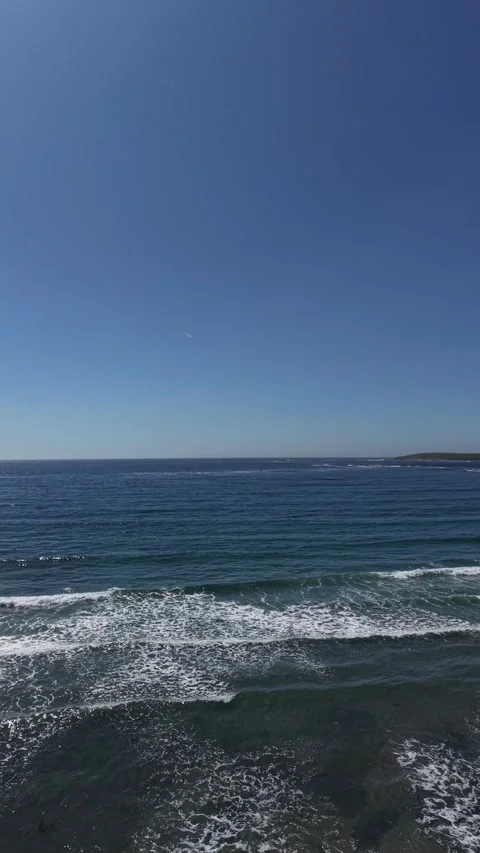 Ocean Waves Breaking on a Sandy Beach Under Clear Blue Sky Video stock 339583699