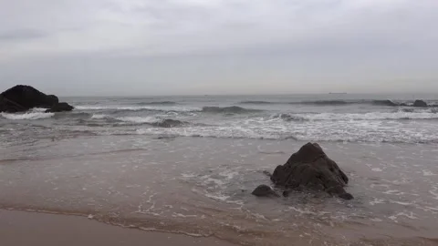Ocean waves breaking on the shore next to a large rock on a cloudy autumn day Stock Footage 338328594