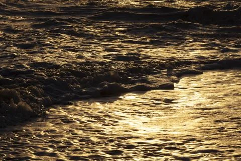 Ocean waves breaking on the shore at sunset, light reflecting off the water. Stock Photos