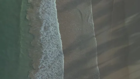 Ocean waves calmly wash over sand beach, top down aerial pull-out Stock Footage 276569450