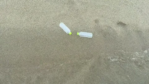 Ocean waves carrying plastic bottles across sandy shoreline. Plastic pollution Video stock 337411881