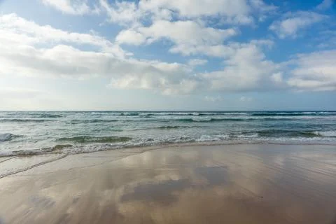 Ocean waves with cloud reflections on wet sand beach. 写真素材