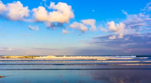 Ocean waves, clouds, moon and blue sky in Legian, Bali 写真素材