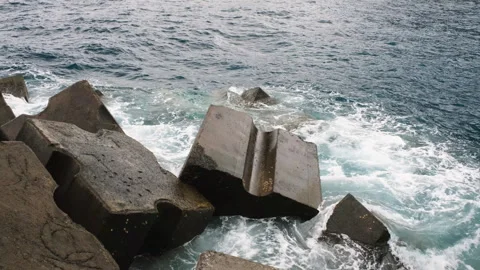 Ocean waves crash against massive concrete tetrapods protecting a rugged Stock Footage 346390312