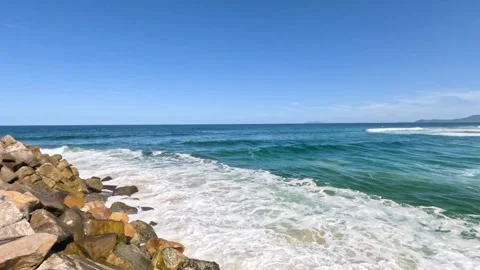 Ocean waves crash against rocks on sunny day, dynamic ocean movement footage. 스톡 동영상 334395556