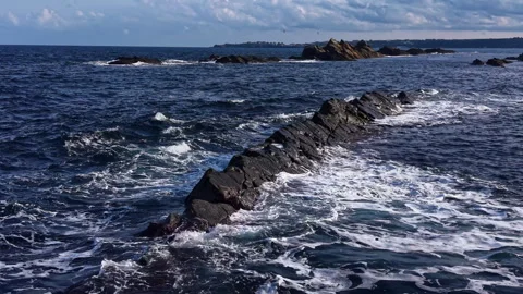 Ocean waves crash against rocky shoreline near distant land during sunny day Stock Footage 331954975