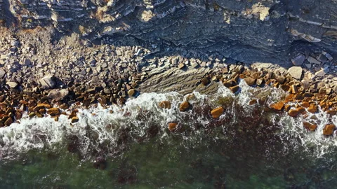 Ocean waves crash against rocky shore under clear sky along coastline during Stock Footage 340855149