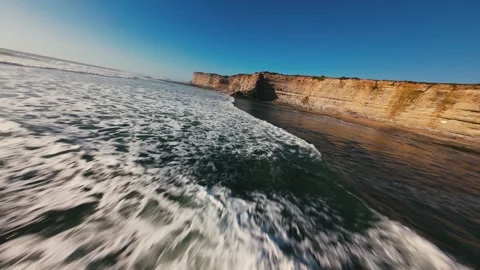 Ocean waves crash against rugged cliffs under clear blue sky Stock Footage 339786462