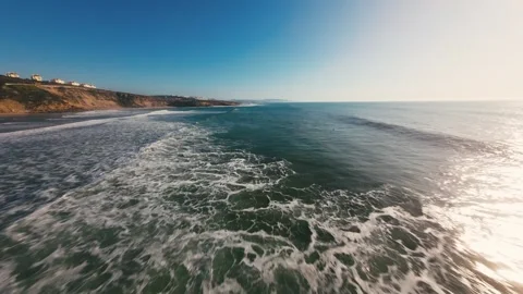 Ocean waves crash against rugged cliffs under bright blue sky Stock Footage 339786628