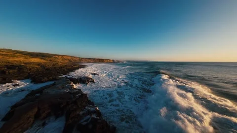 Ocean waves crash against rugged cliffs under golden sky Stock Footage 339788361