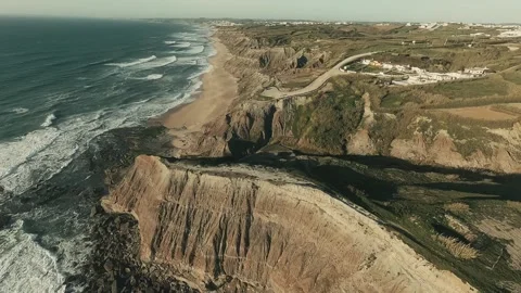 Ocean waves crash against rugged cliffs beneath clear skies Video stock 341826804
