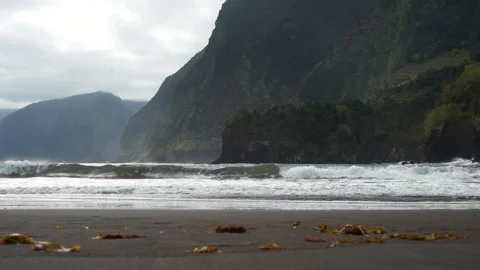 Ocean Waves Crash on Black Sand Beach Beneath Towering Cliffs Stock Footage 334592469