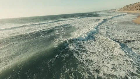 Ocean waves crash on golden sands below rocky cliffs Stock Footage 341826906