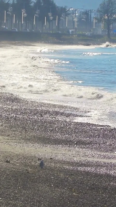 Ocean waves crash on pebble beach shore sunny day Stock Footage 334185700
