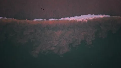 Ocean waves crash onto sandy shore, creating foam and swirling patterns Video stock 337418829
