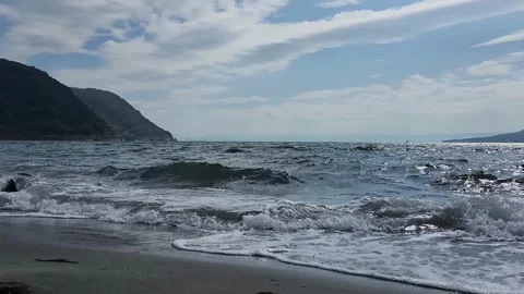 Ocean waves crash onto sandy shore with a prominent rock 動画素材 337696996