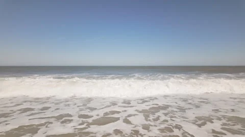 Ocean waves crash in slow motion, rhythmically on sandy shore under clear blue Stockbeeldmateriaal 337180695