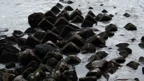 Ocean waves crash on the triangular and checkered rocks that line the ocean Stock Footage 203866719