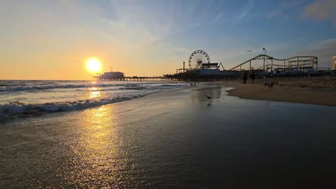Ocean waves crash under Santa Monica Pier at sunset, golden sunlight shines 库存影片 333837889