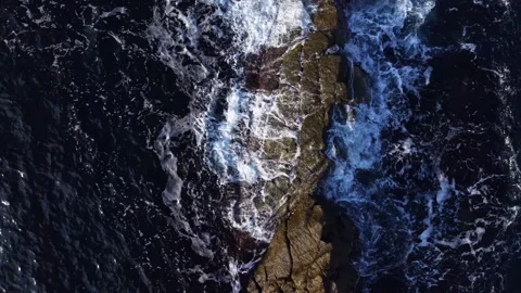 Ocean waves crashing against rugged rocks in a serene coastal landscape at dusk Stock Footage 335372361