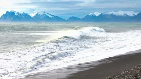 Ocean waves crashing on black sand beach with snowy mountain background. Stock Footage 341132446
