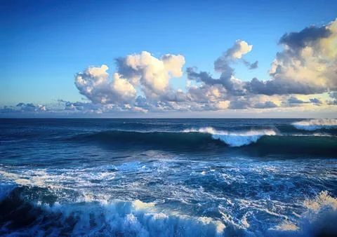 Ocean waves crashing with clouds in a bright sky Stock Photos