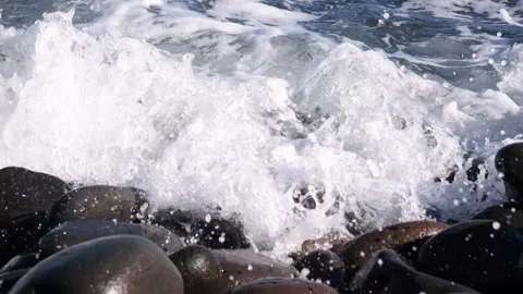 Ocean waves crashing over smooth, wet volcanic stones and covering the rocky Stock Footage 345840889