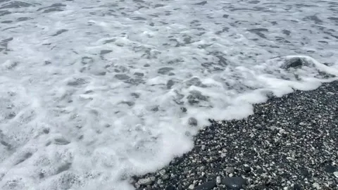 Ocean waves crashing on a pebble beach with a large rock in the water 库存影片 334163081