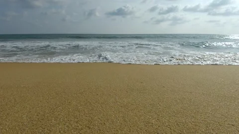 Ocean waves crashing on a sandy beach under a cloudy sky on a sunny summer day Stockbeeldmateriaal 307416451