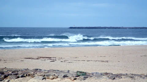 Ocean Waves Crashing on Sandy Beach with Distant Lighthouse Stock Footage 321889895
