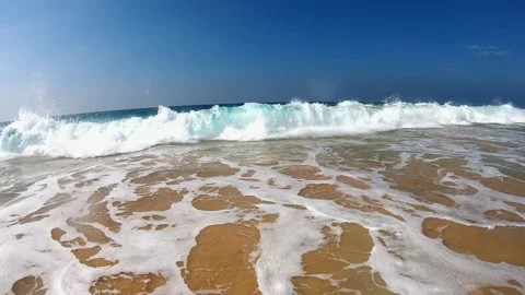 Ocean waves crashing onto sandy shore, creating frothy white foam, with sunlight Video stock 319528243
