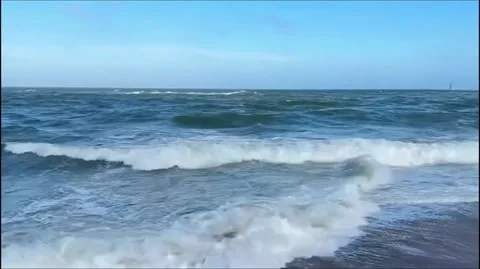 Ocean waves crashing on the shore under a clear blue sky on a windy day Vidéo 334163716
