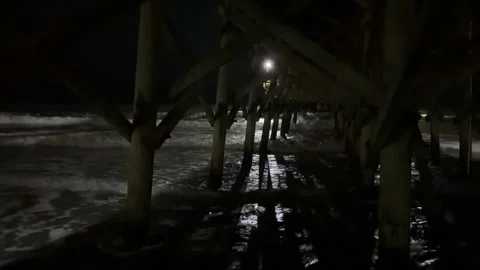 Ocean Waves crashing under the pier at night with the moonlight shining through. Stock Footage 337479300