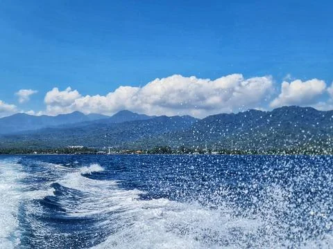 Ocean waves create a dynamic scene with mountains visible in the distance und Stock Photos