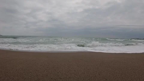 Ocean waves gently crash onto a sandy beach beneath a dramatic cloudy sky. Vidéo 333029196