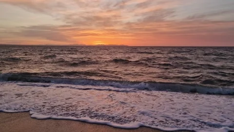 Ocean waves gently lap against a sandy shore under a dramatic sky Stock Footage 334999985