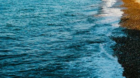 Ocean waves gently lapping against pebbled beach at sunset Stock Photos