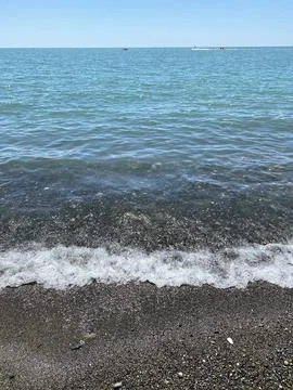 Ocean waves gently lapping onto pebble beach on sunny day, perfect for back.. Stock-Fotos