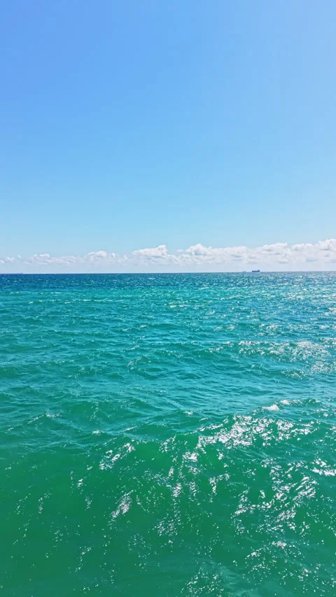 Ocean waves gently rolling under a clear blue sky with a few clouds in the Видео 346983082