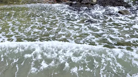 Ocean waves gently washing up onto a rocky beach creating beautiful pattern.. Video stock 332629801