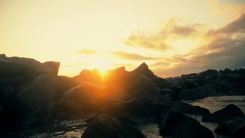 Ocean waves hitting across huge stones with birds flying over during the sunset. Видео 106849179