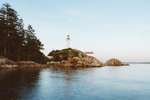 Ocean waves hitting rocks on coast and lighthouse in background while sunset Stock Photos