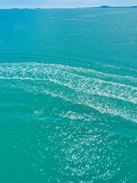 Ocean waves move across the turquoise water near a coastline under a clear .. Stock Photos