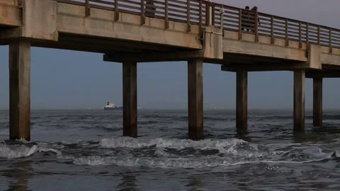 Ocean waves, a pier at dusk, a distant ship going out to sea, and walkers. Stock Footage 236951714