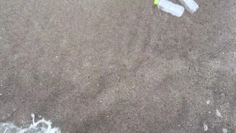 Ocean waves pull discarded plastic bottles from sandy beach into sea, spreading Видео 337411867