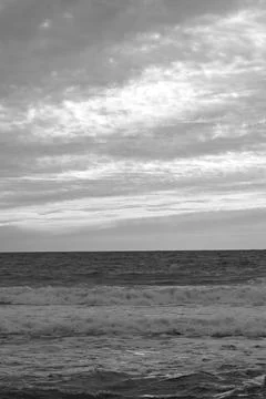 Ocean waves roll beneath layered sunset clouds Stock Photos