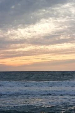 Ocean waves roll beneath layered sunset clouds Stock Photos