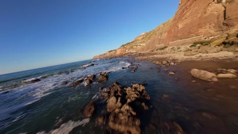 Ocean waves roll over rugged coastlines with red-brown cliffs Stock Footage 344557109