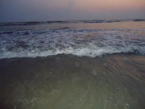 Ocean waves roll onto the shore during a dusky pastel colored evening Stock Photos
