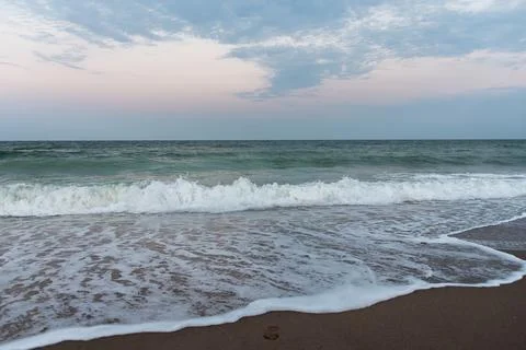 Ocean waves rolling onto foamy sandy shore under pastel evening sky Stock Photos